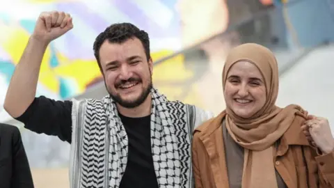 Khalil holds his fist up while standing with his wife